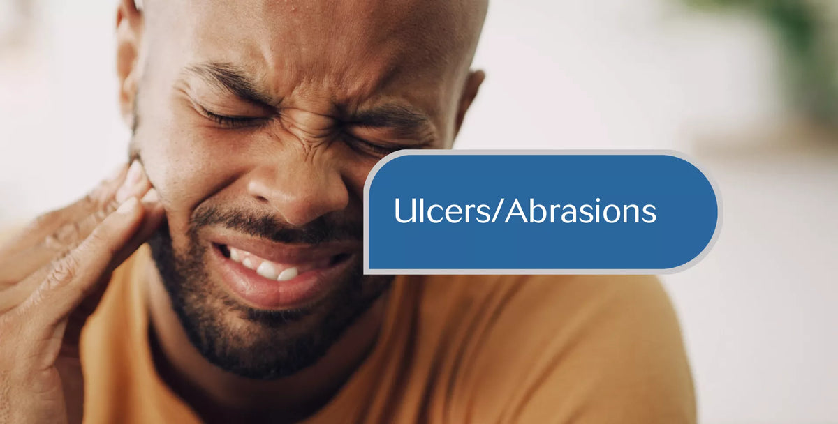 A close-up of a man grimacing in discomfort while holding his ear, with a blue label overlay reading 'Ulcers/Abrasions' on a softly blurred indoor background.